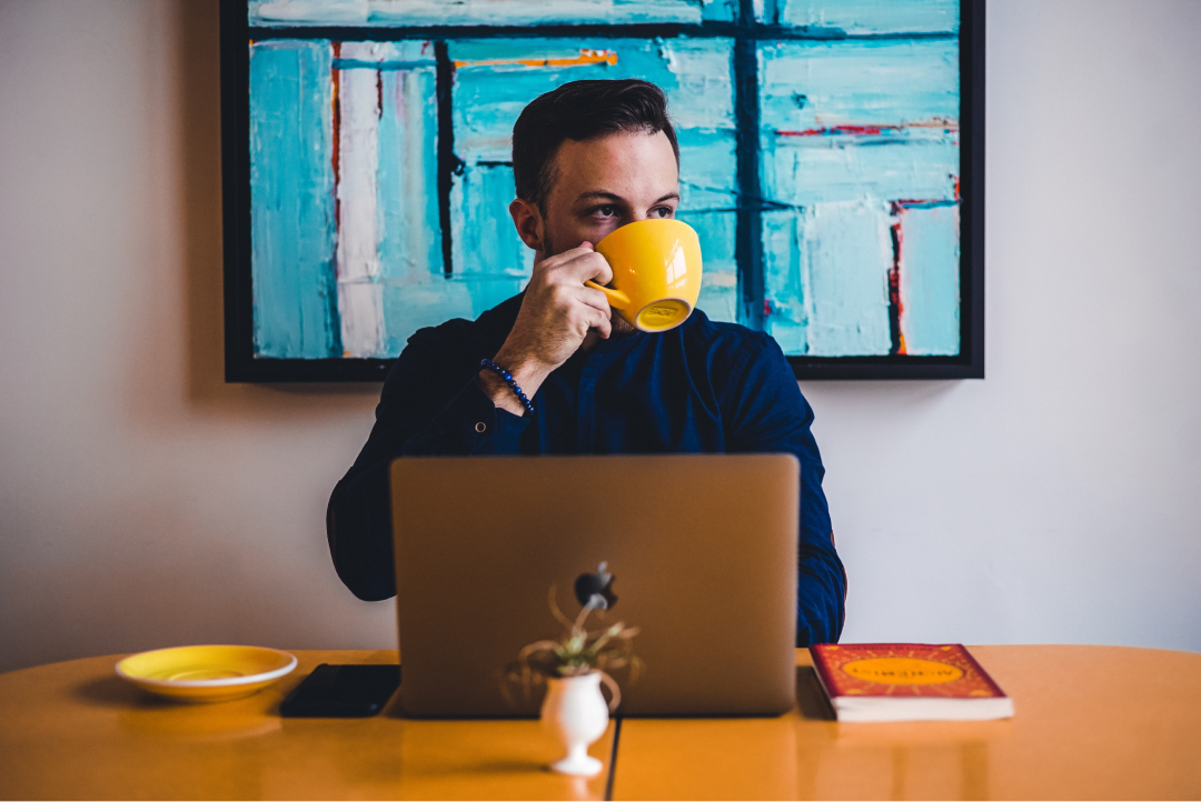 A man drinks coffee in front of his laptop in a coffee shop